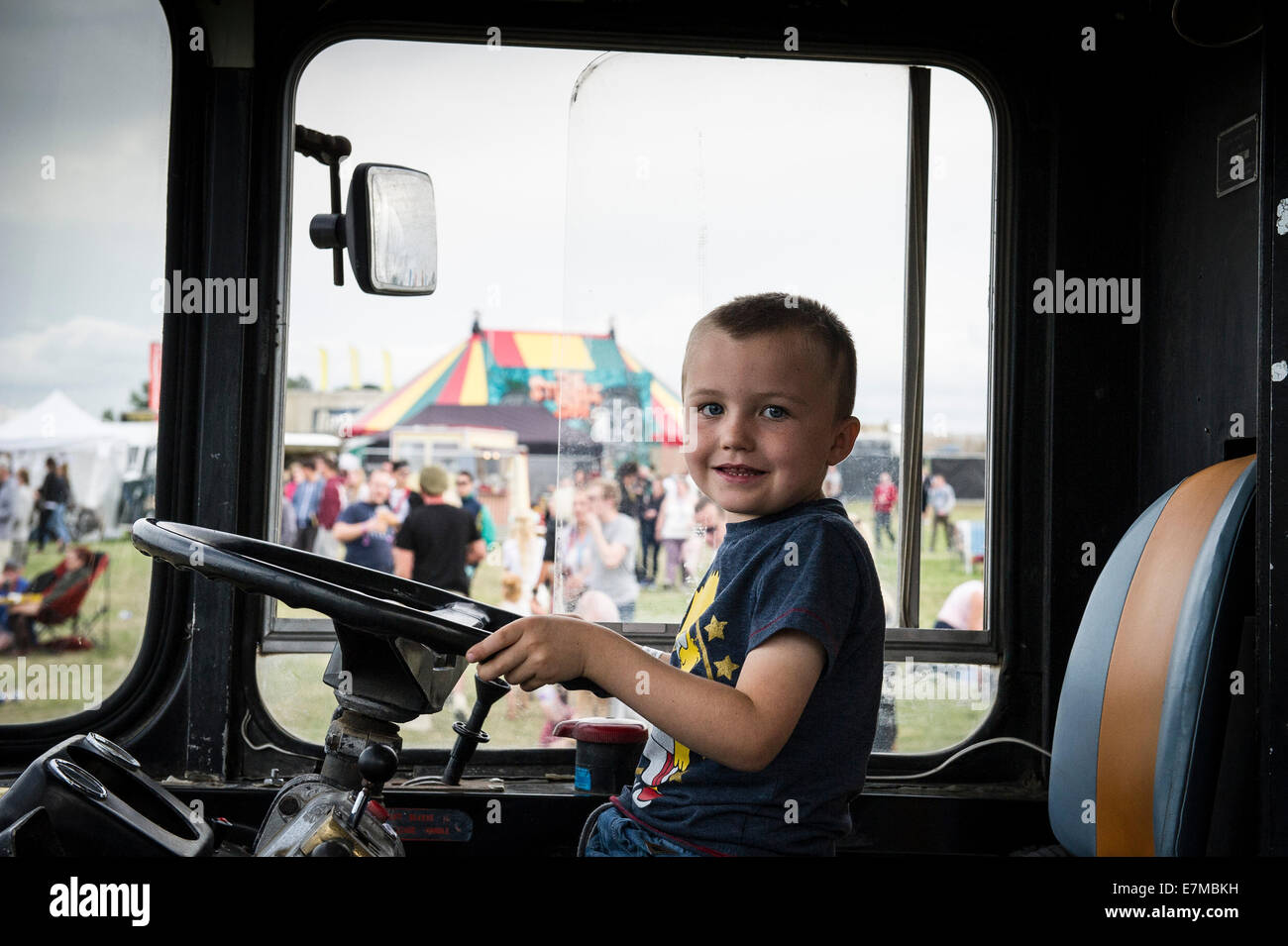 A young lad sitting inn the driver's seat of the Party Bus at the Brownstock Festival in Essex. Stock Photo