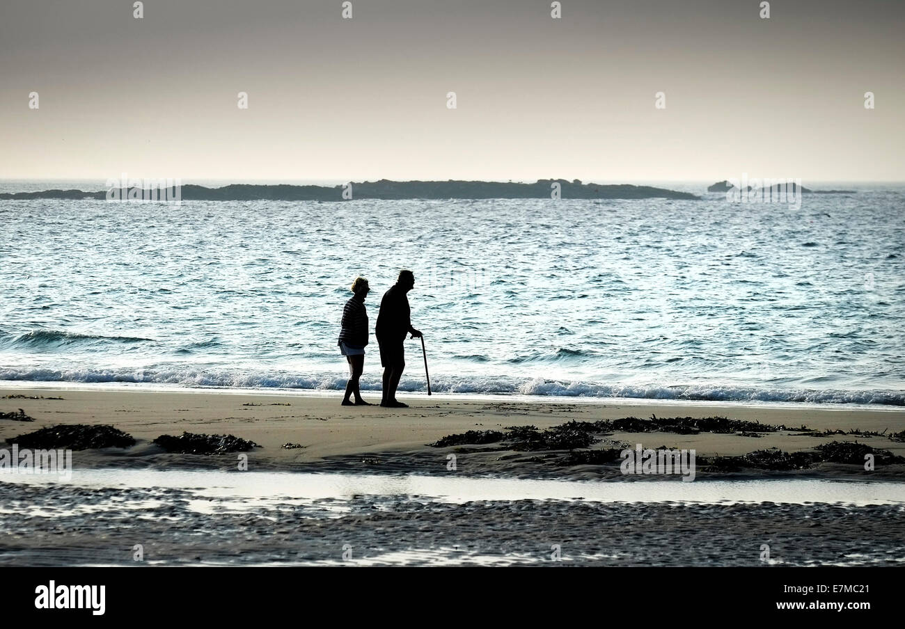 Two people seen in silhouette walking along the shore at Sennen Cove in Cornwall. Stock Photo