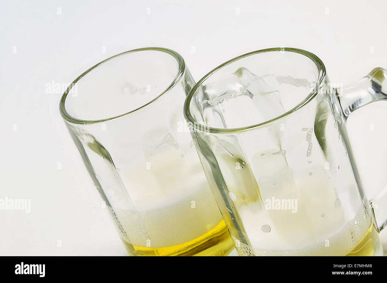 two beer mugs with beer and foam, half full, half empty, on white background, diagonal Stock Photo