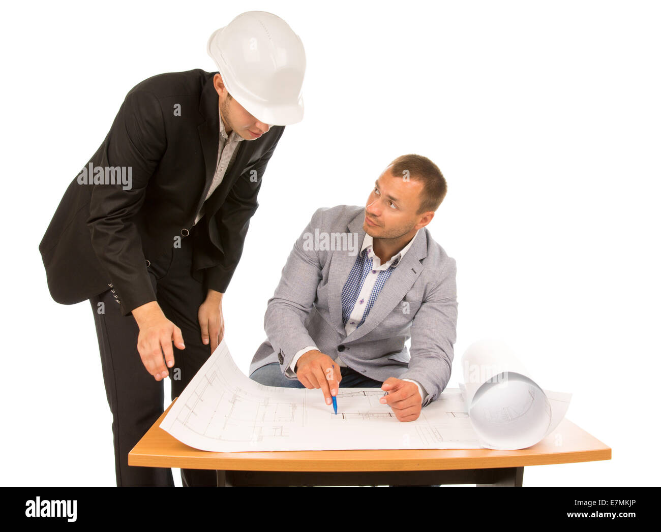 Building foreman and architect discussing a plan or blueprint with one standing looking down and the other seated pointing to a  Stock Photo