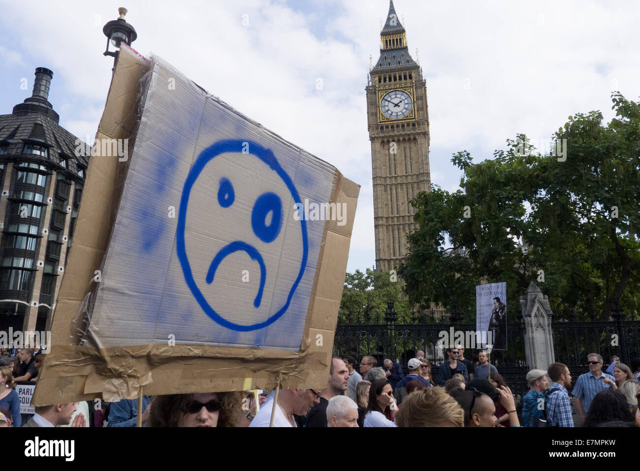 A protester holds a cardboard placard with a grumpy face and a black eye as she passes the tower of Big Ben during the Climate Change demonstration, London, 21st September 2014. © Sue Cunningham Stock Photo
