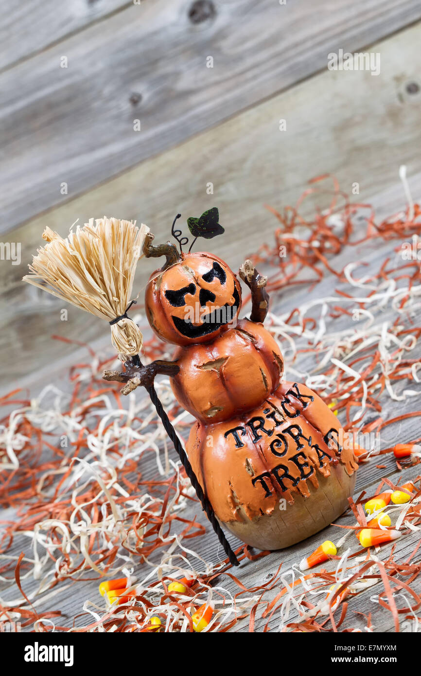 Vertical angled image of a scary orange pumpkin figure holding straw broom placed on rustic wooden boards Stock Photo