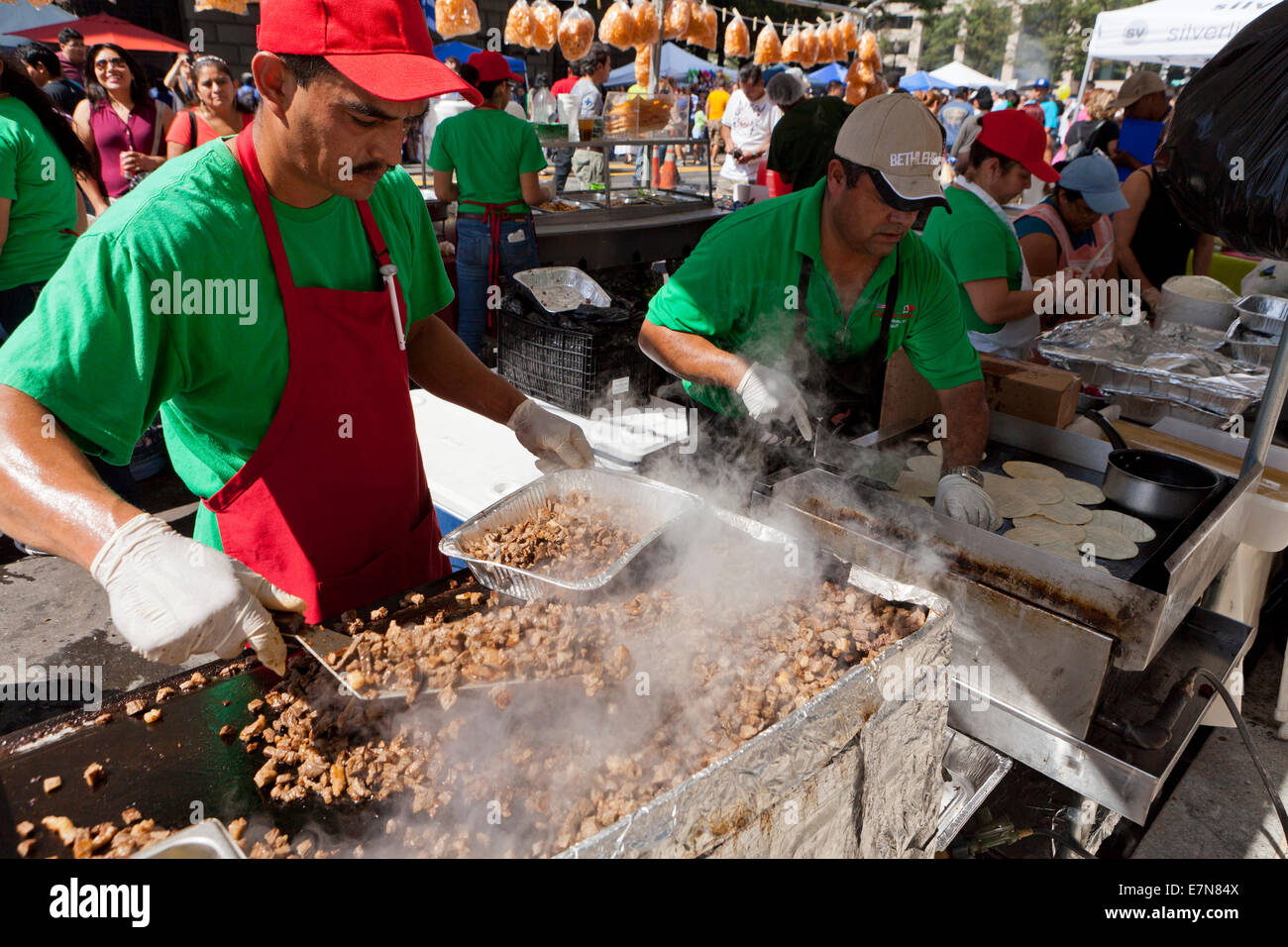 Man grilling chopped pork meat on large griddle at an outdoor food festival - USA Stock Photo