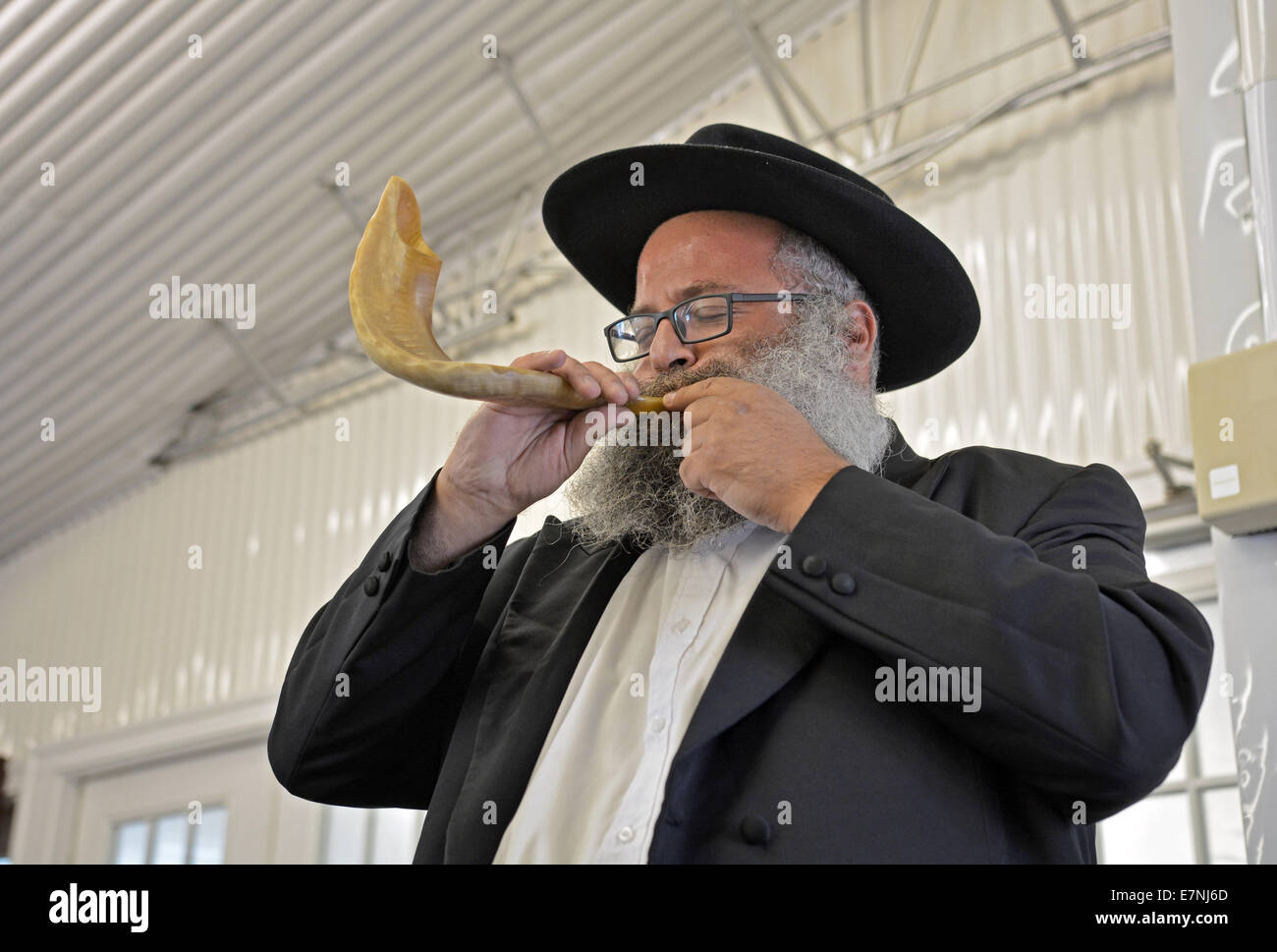 Religious Jewish man blows a shofar during services prior to New Year in a synagogue in Cambria Heights, Queens New York Stock Photo