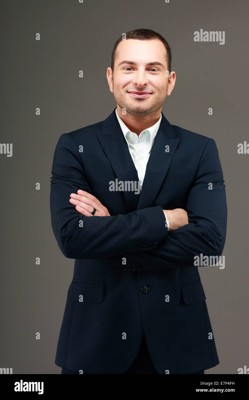 Portrait of smiling businessman with arms folded on gray background ...