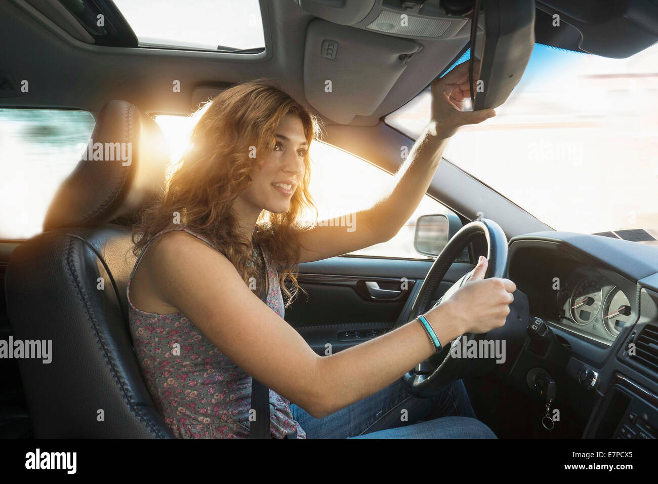 Young woman adjusting rear view mirror while driving Stock Photo