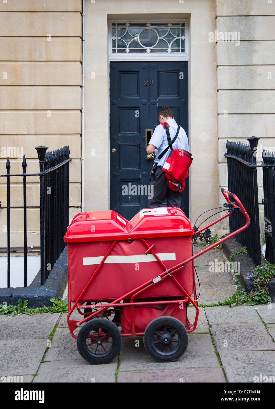 Postman delivering letter and mail through a Bristol house front door with the aid of a red mail cart Stock Photo