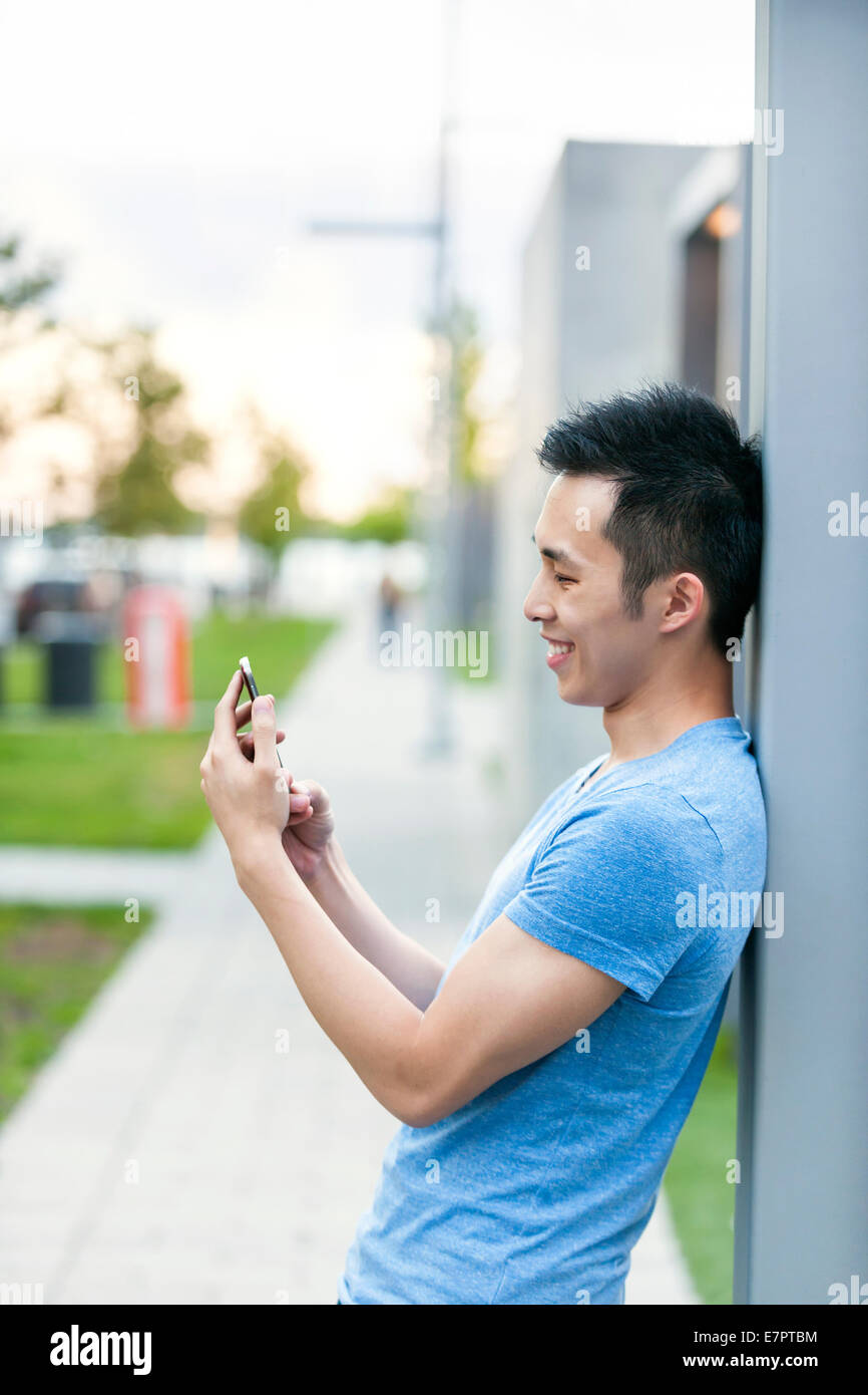 Young asian man smiling and looking at smart phone on city sidewalk ...