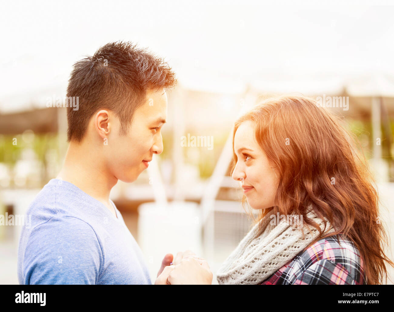 Romantic interracial young couple holding hands and looking at each other outside in sunset light Stock Photo