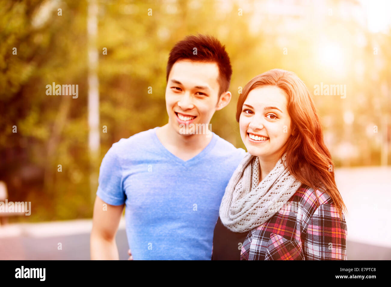 Romantic interracial young couple standing together and looking at camera outside in sunset light Stock Photo