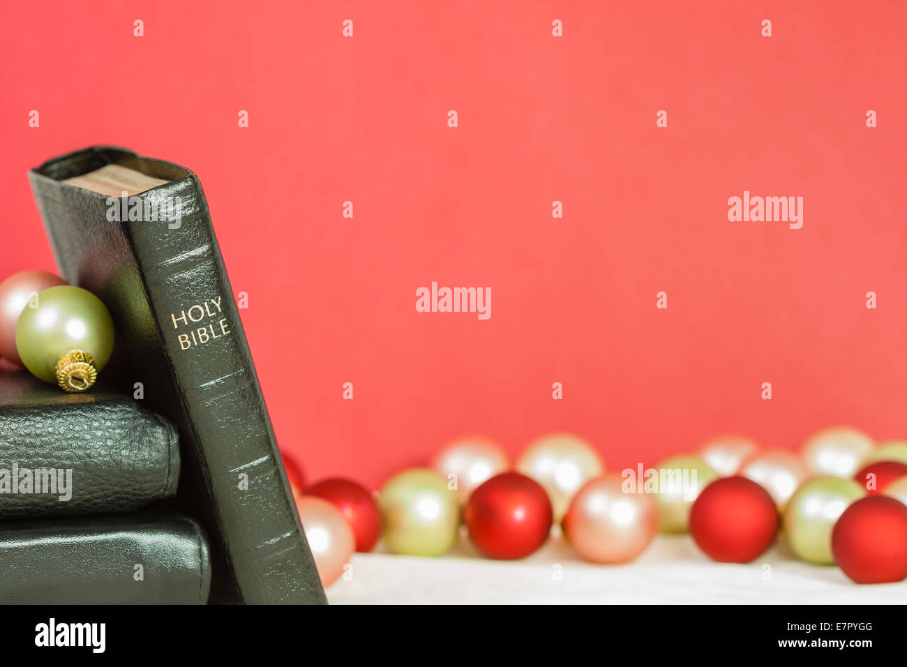 A sharply focused Holy Bible with Christmas ornaments against a red background. Can be used for Christmas Bible passages. Stock Photo
