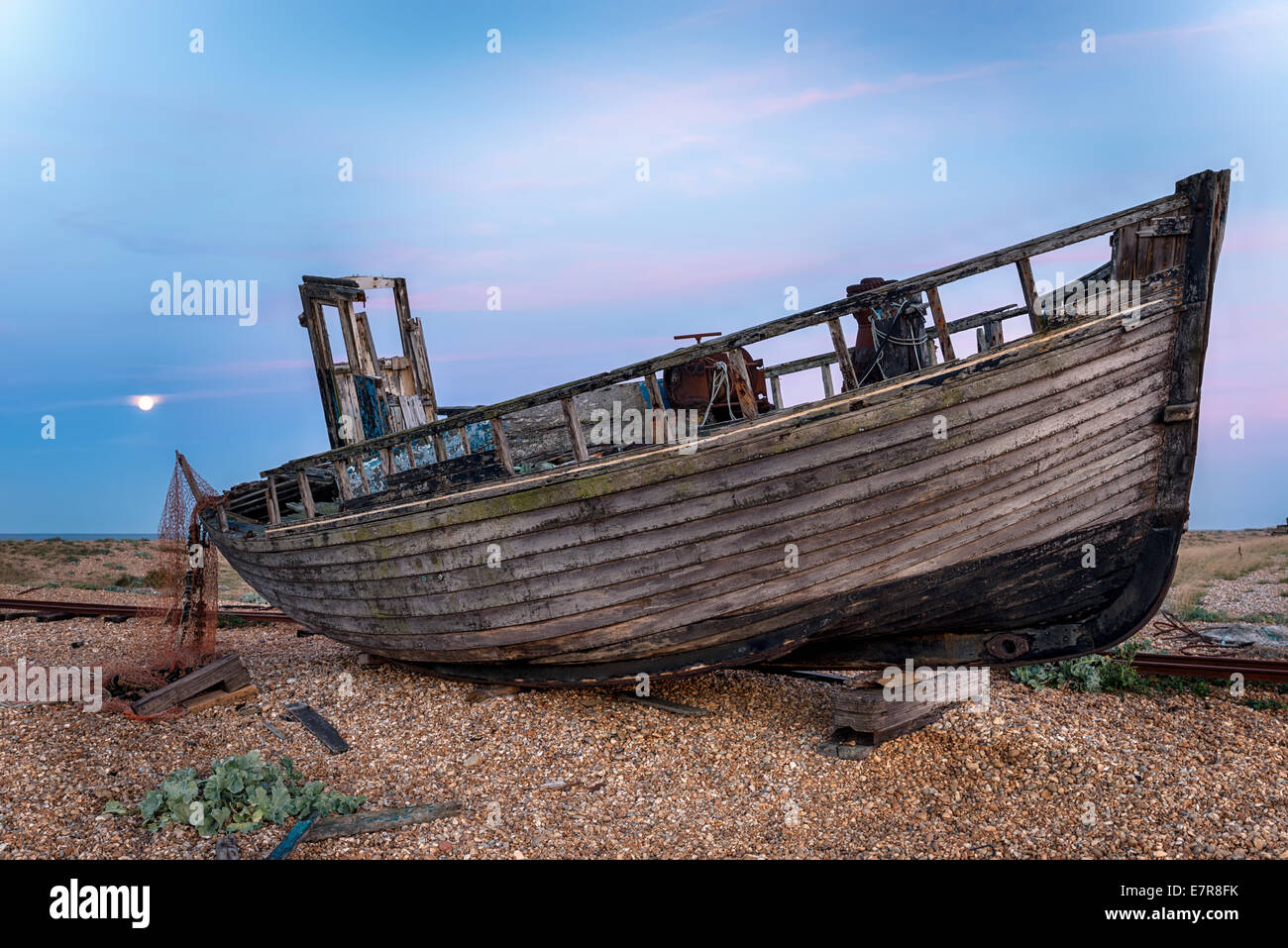 An old wrecked wooden fishing boat on a shingle beach under the light of a full moon Stock Photo