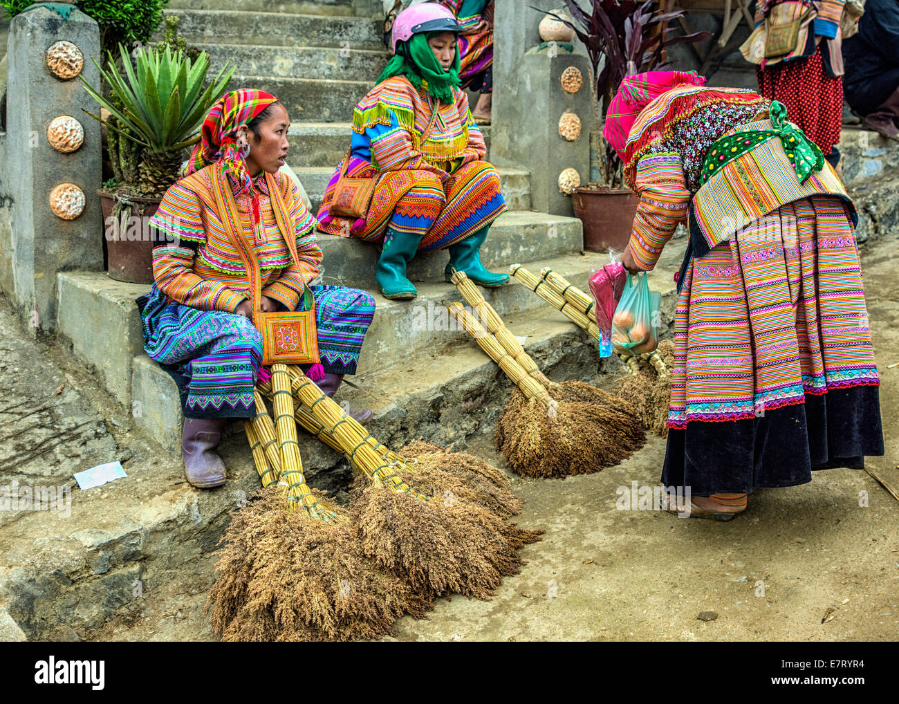 Hmong women in colorful dress sell brooms on Sunday market. Stock Photo