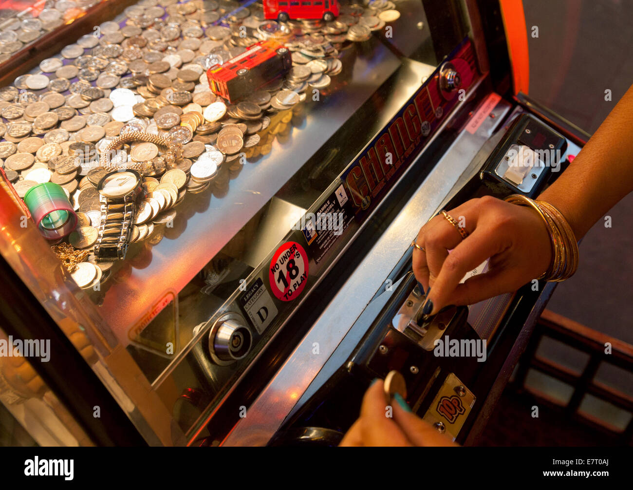 Women putting coins into a gambling machine in an amusement arcade, London UK Stock Photo