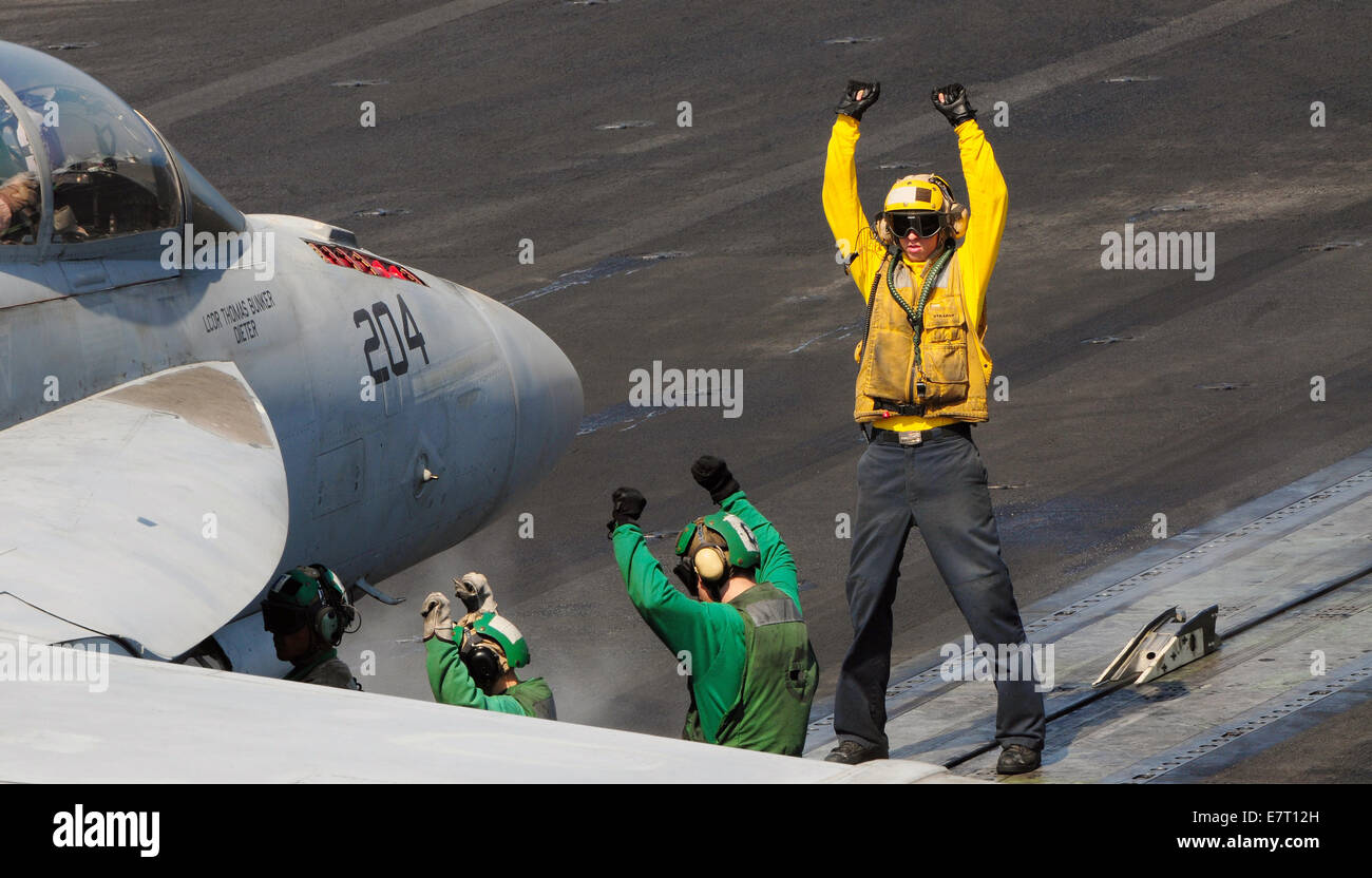 A US Navy sailor on the flight deck crew directs a F/A-18F Super Hornet fighter aircraft during flight operations from the aircraft carrier USS George H.W. Bush September 22, 2014 in the Persian Gulf Sept. 22, 2014. The military launched the first direct strikes on ISIS targets inside Syria. Stock Photo