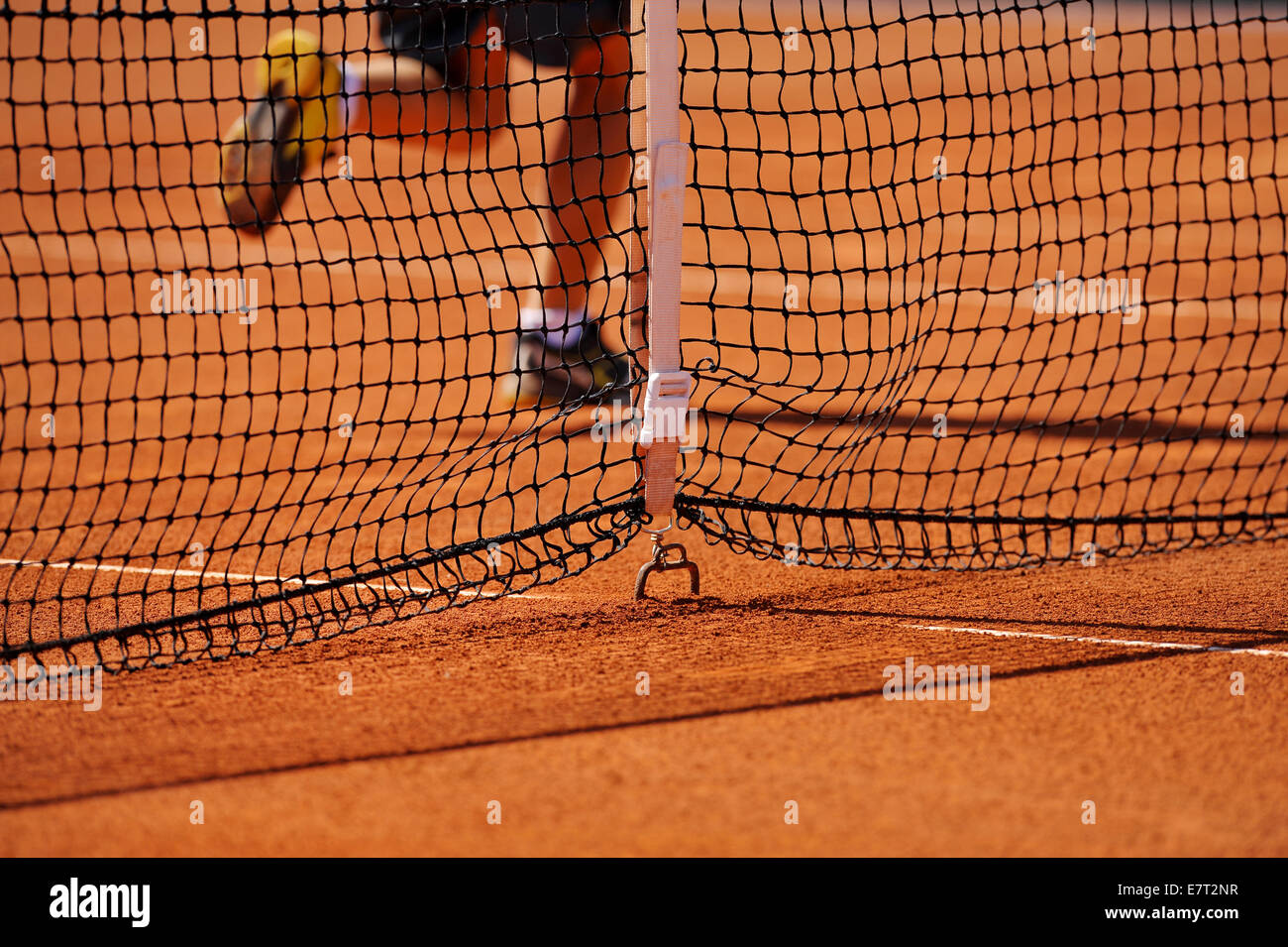 Tennis net detail on a clay court with a ball boy running in background