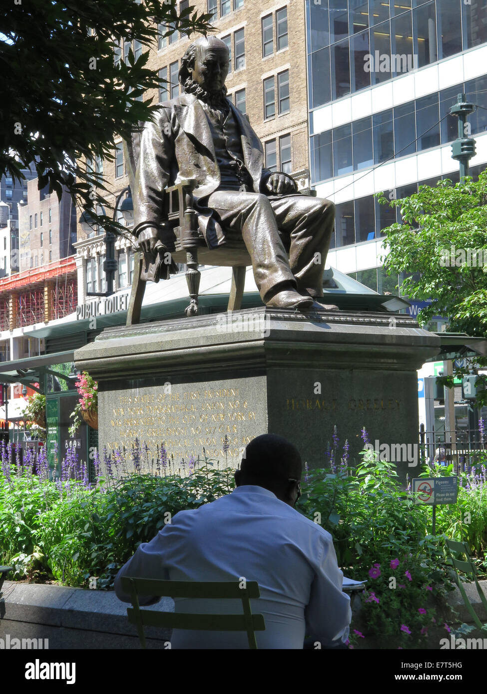 Statue of Horace Greeley on a summer day in Greeley Square, New York City. Tables and chairs surround the statue. Stock Photo
