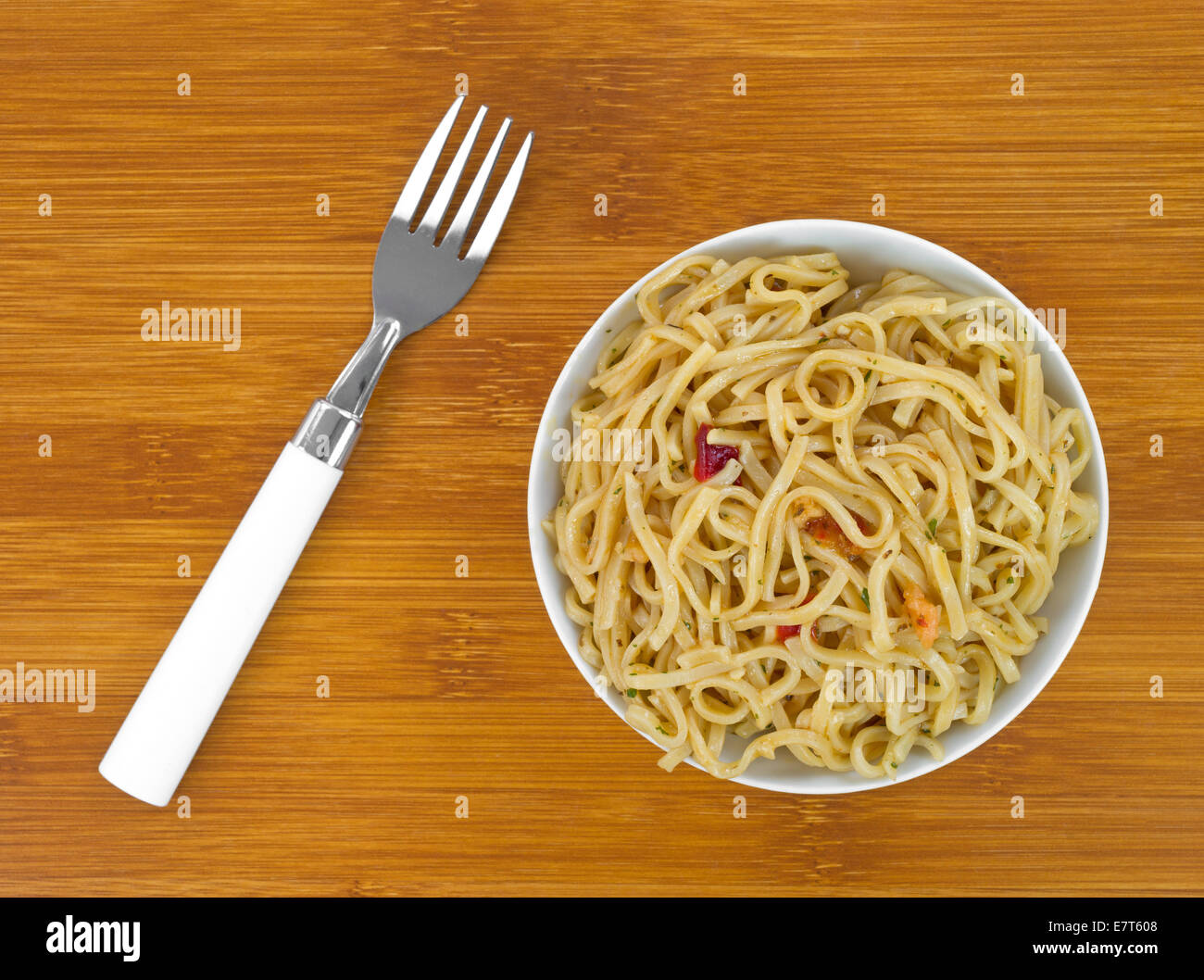 Top view of a serving of Chow Mein noodles with shrimp and seasonings in a small bowl with a fork to the side on a wood table to Stock Photo