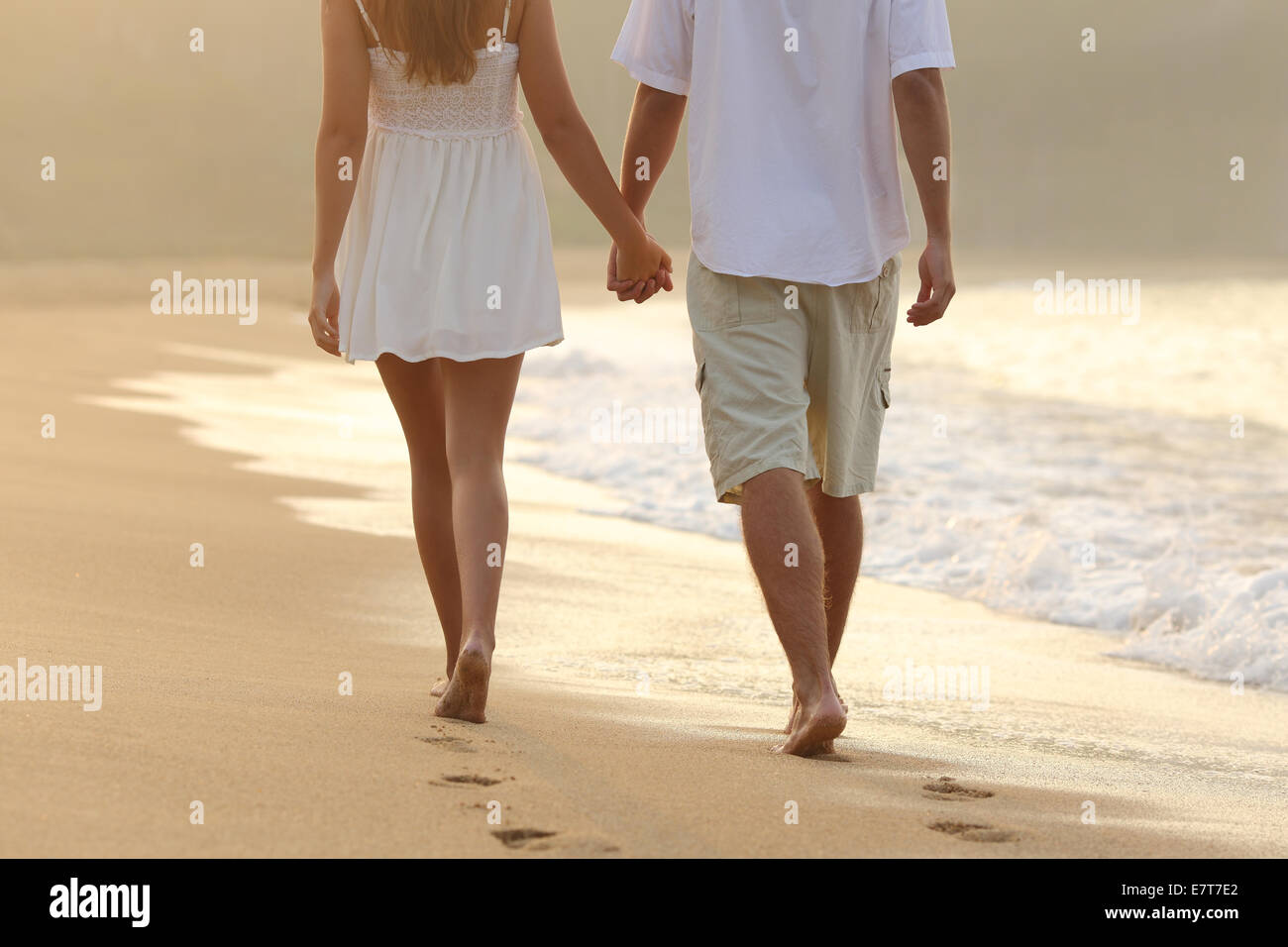 Back view of a couple taking a walk holding hands on the beach at sunrise Stock Photo