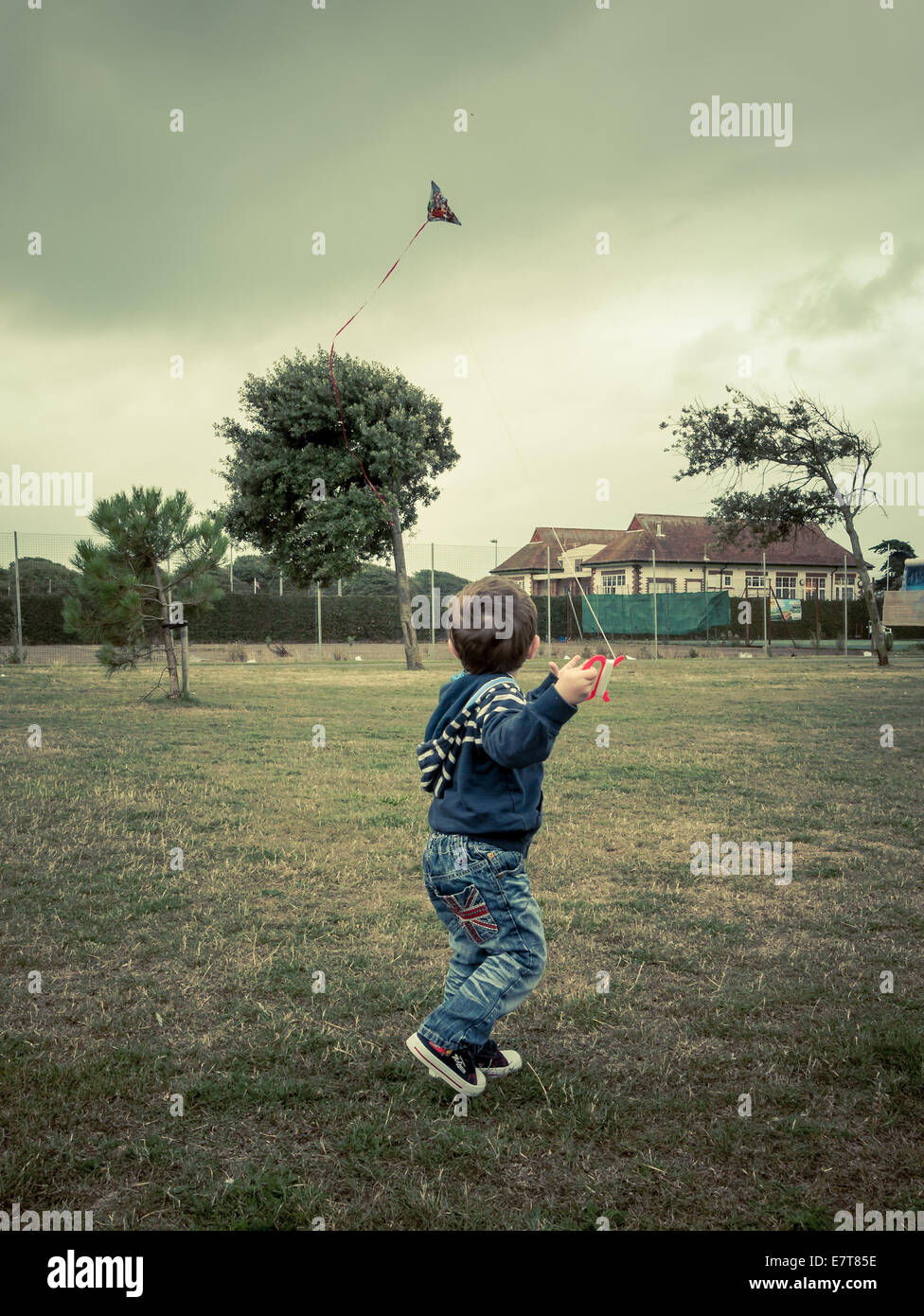 young boy flying a kite in windy weather with dark clouds Stock Photo