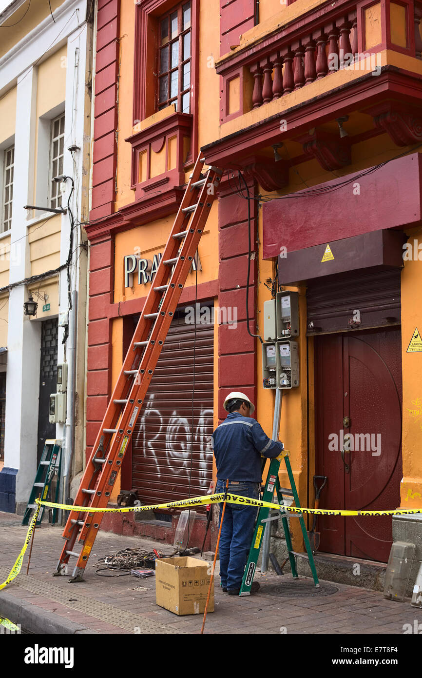 Unidentified man with safety helmet standing at electricity meters beside a ladder and tools in Quito, Ecuador Stock Photo