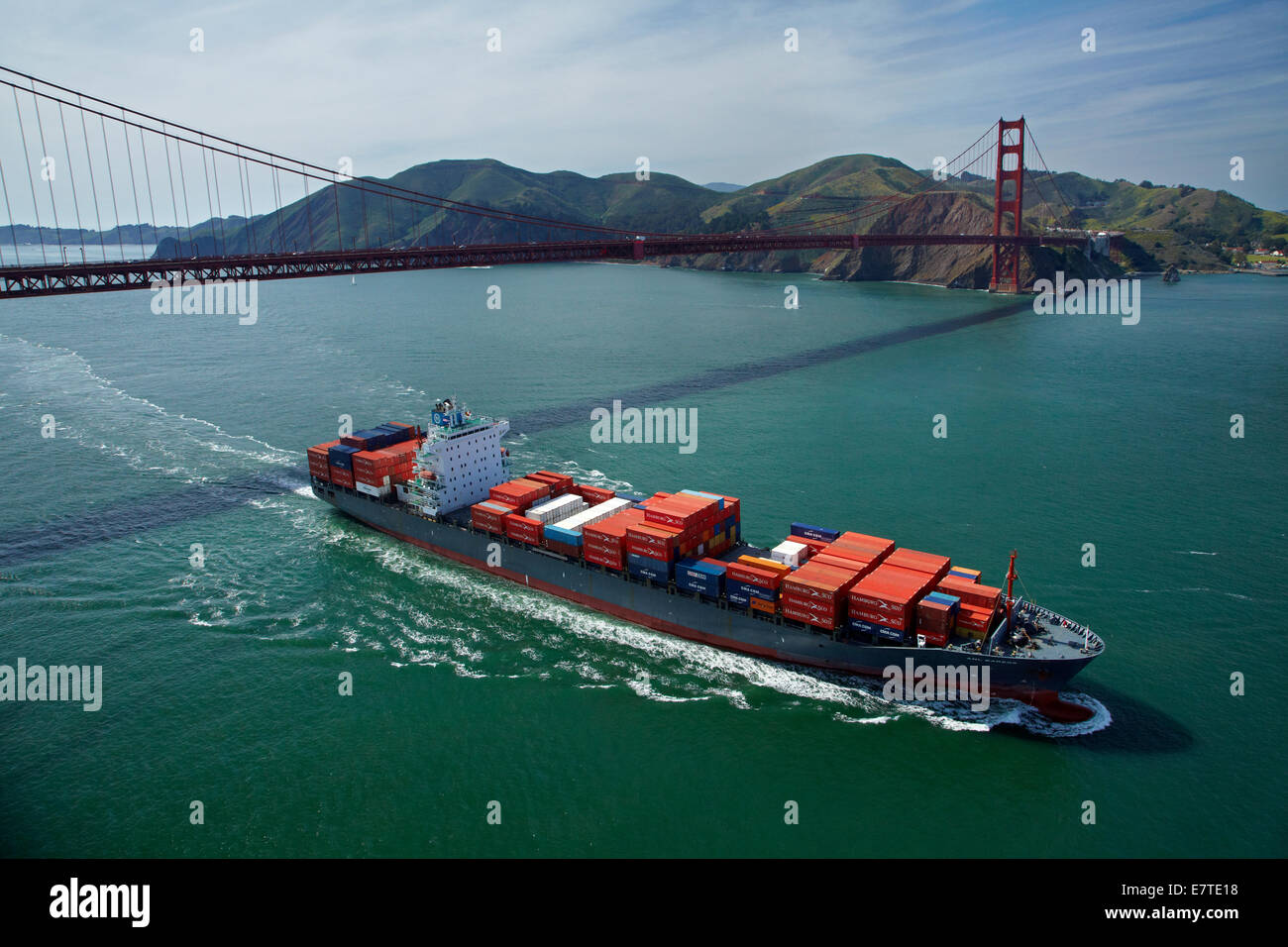 Container ship passing under Golden Gate Bridge, and Marin Headlands, San Francisco Bay, San Francisco, California, USA - aerial Stock Photo