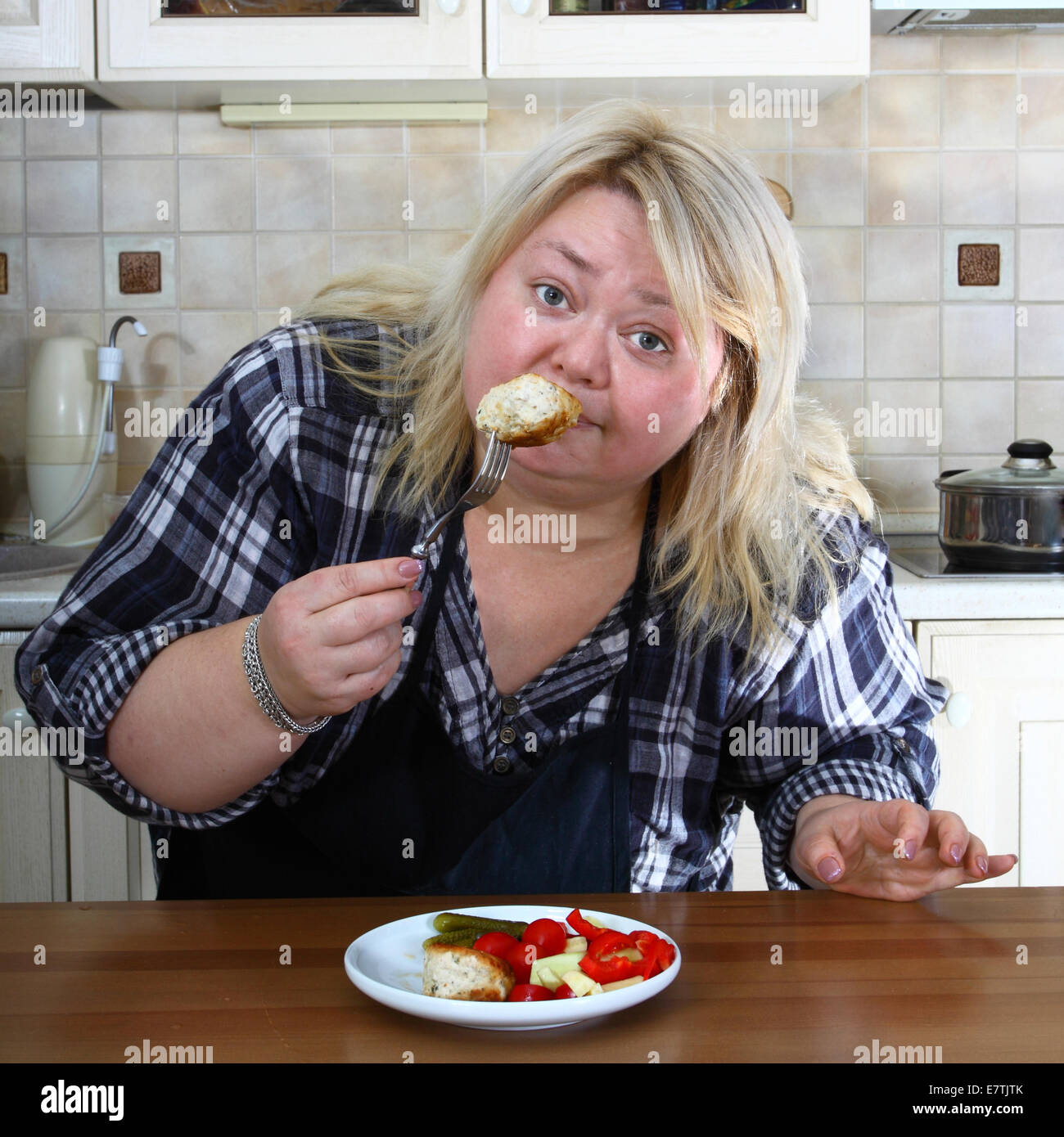 Big woman in kitchen tastes a cutlet Stock Photo
