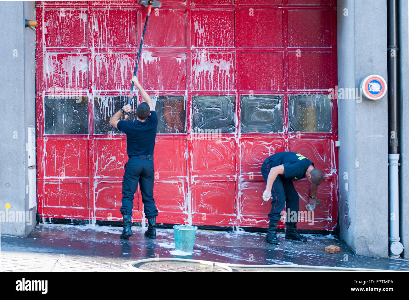 Two Parisian fireman wash the door to the firehouse Stock Photo