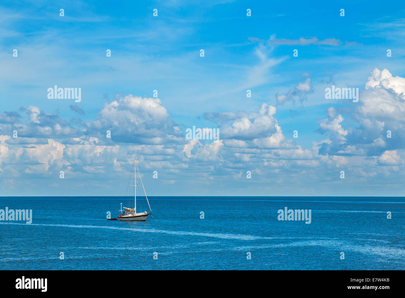 Isolated sailboat on blue ocean sea with white fluffy clouds in clear blue sky looking restful relaxing calm isolated secluded p Stock Photo