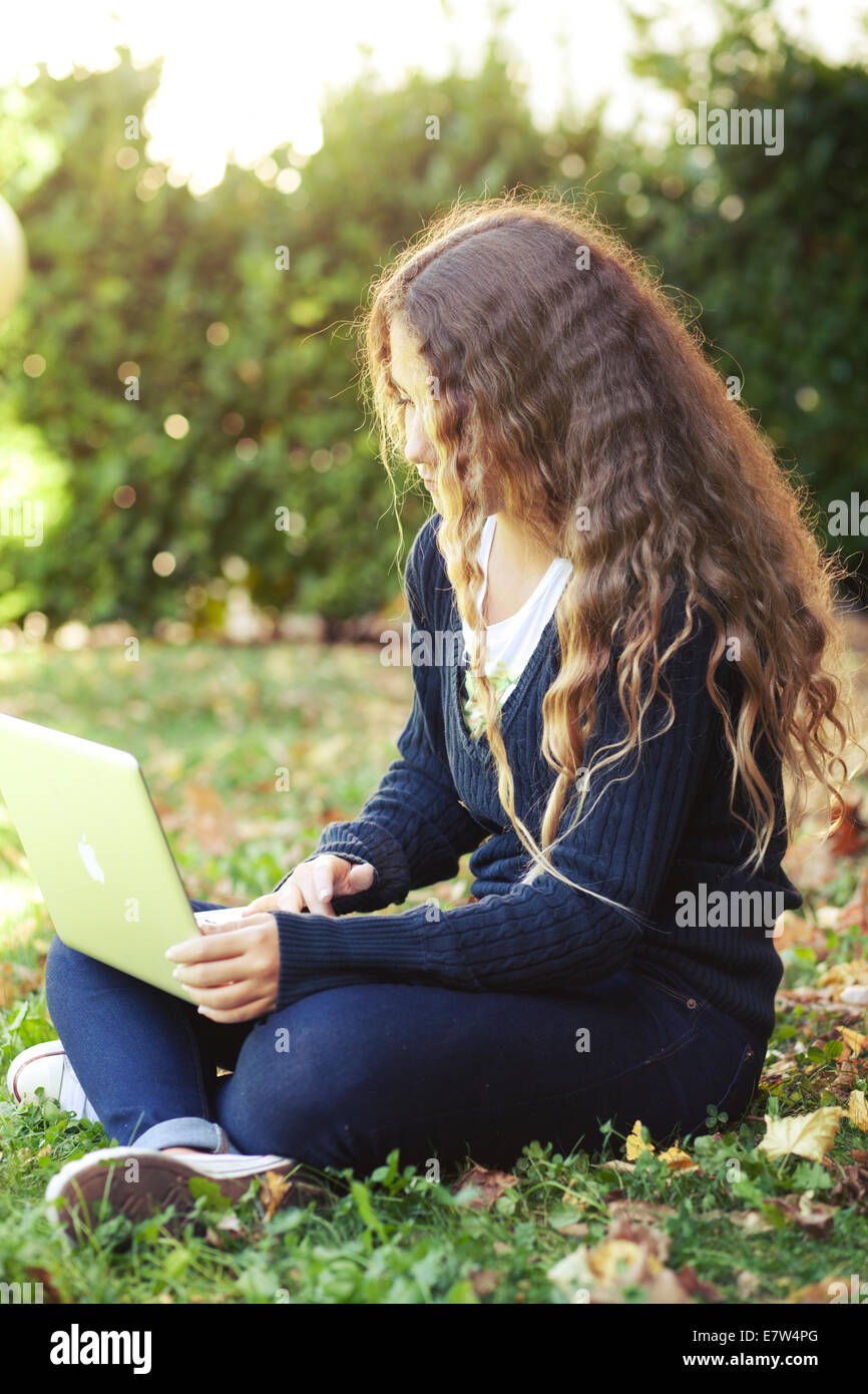 Teenager female girl student with laptop outdoor in the garden with fallen leaves. Autumn Stock Photo