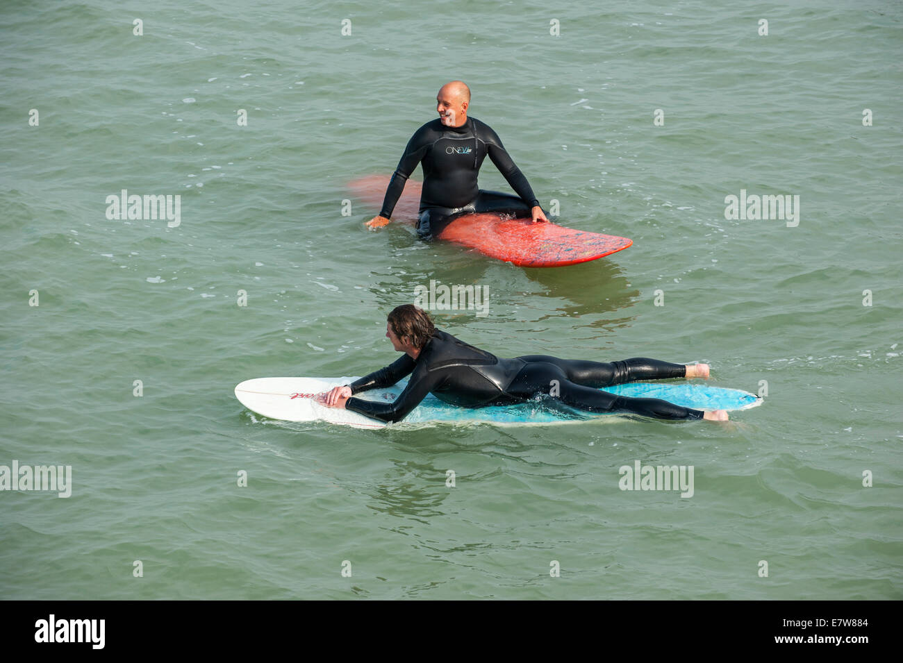 Two surfers in wetsuits waiting on their surfboards for a big wave