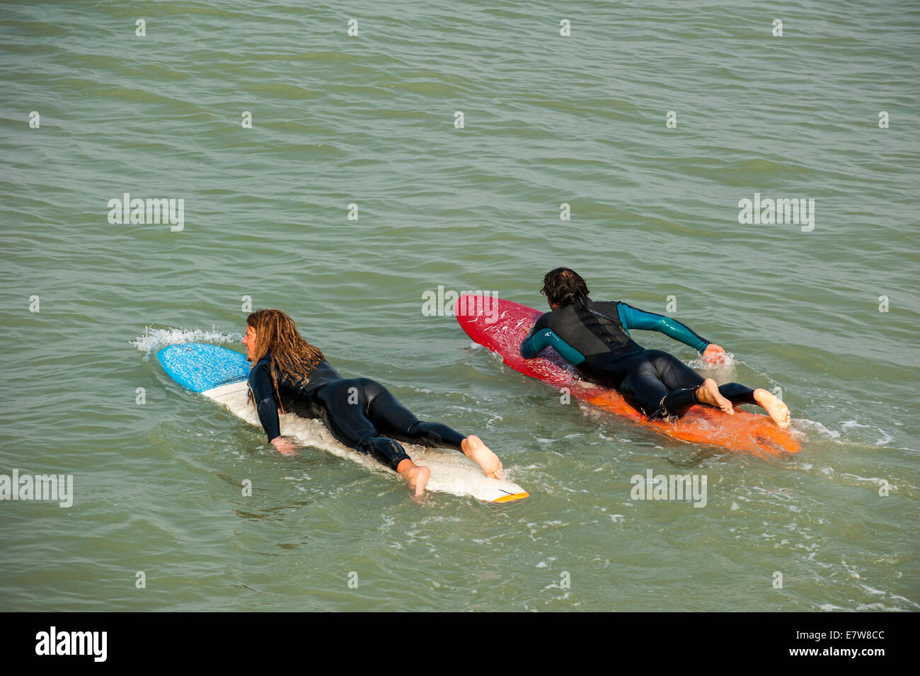 Two surfers in wetsuits laying flat on their surfboards in the sea