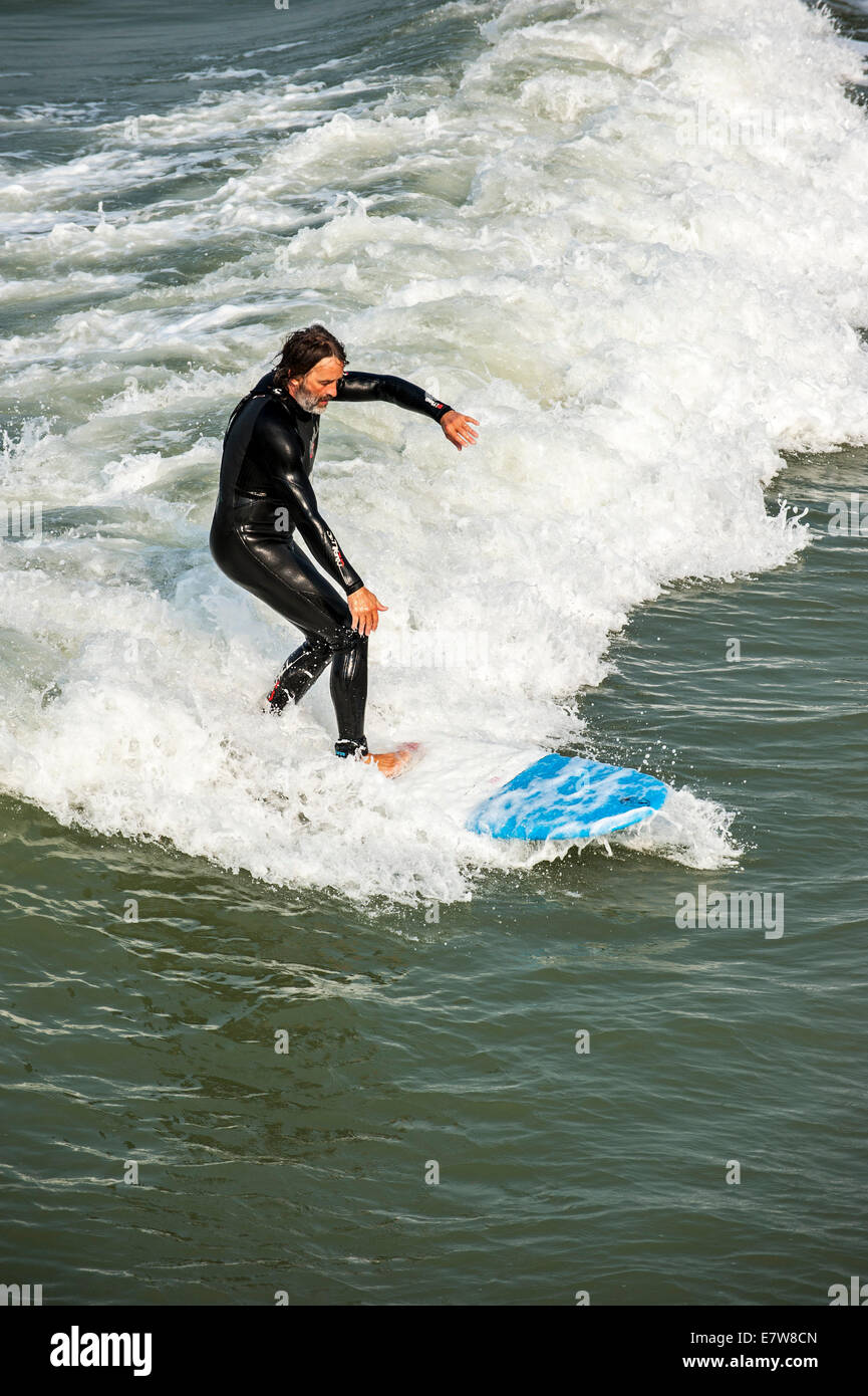 Middle aged surfer in wetsuit riding a wave on surfboard on the North Sea Stock Photo