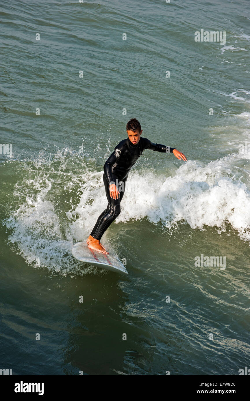 Young surfer in wetsuit riding wave on surfboard as it breaks at sea Stock Photo