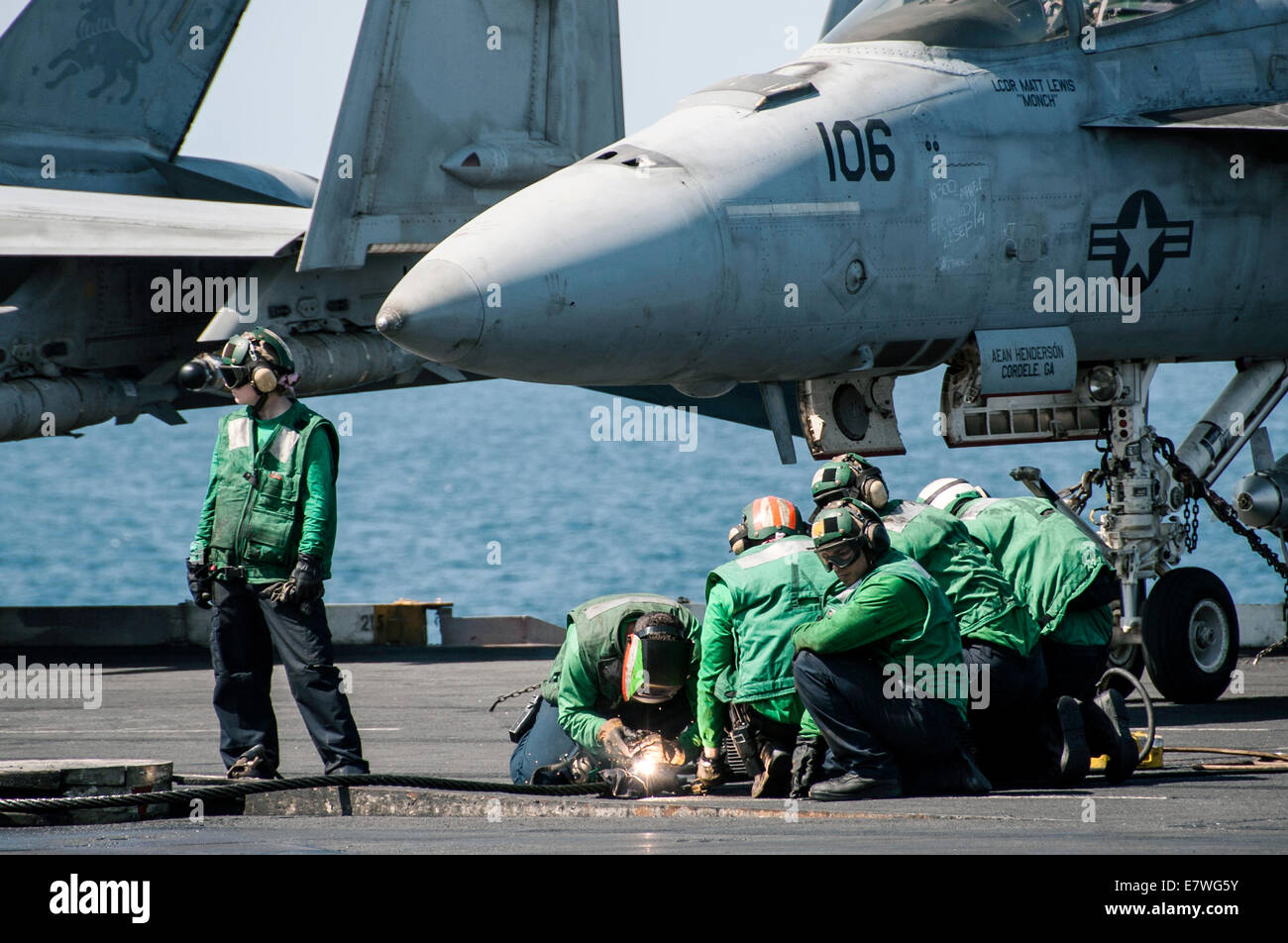 US Navy sailors perform maintenance on arresting gear on the flight deck of the aircraft carrier USS George H.W. Bush September 23, 2014 in the Persian Gulf. The military launched the first direct strikes on ISIS targets inside Syria. Stock Photo