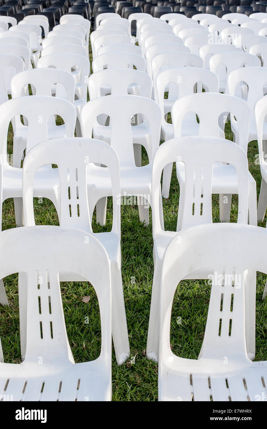 White plastic stackable lawn chairs in rows waiting for a crowd Stock Photo