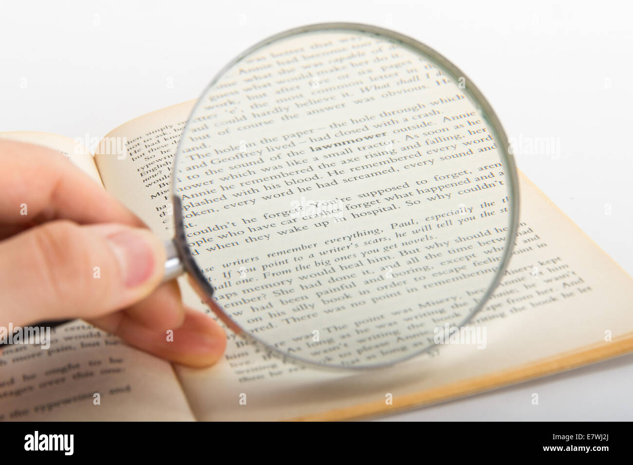 Hand holding classic style magnifying glass and examining reading book, isolated on white background. Stock Photo