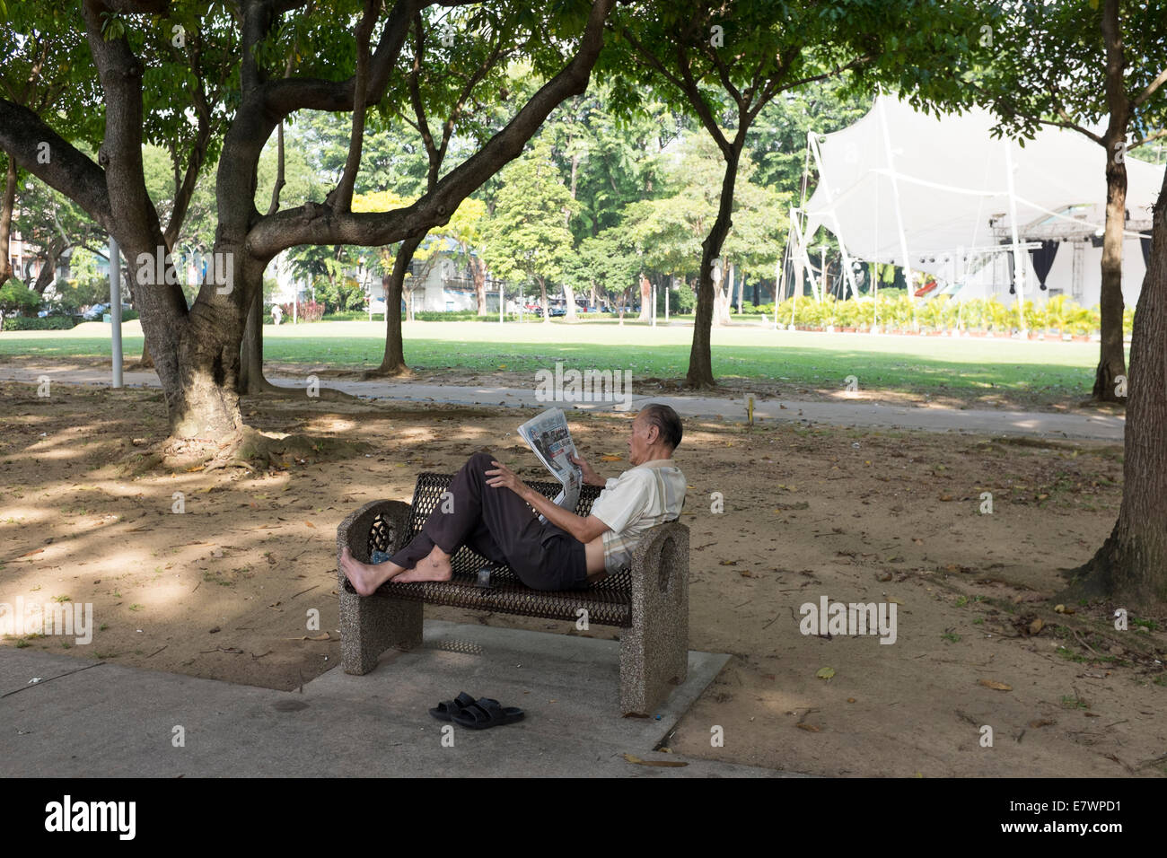 An elderly man takes reads a newspaper in a Hong Lim park in Singapore. Stock Photo