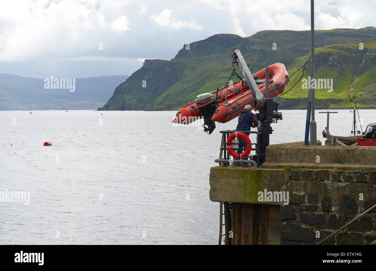 A man lowering a small inflatable boat at Portree Harbour on the Isle Of Skye, Scottish Highlands, Scotland. Stock Photo