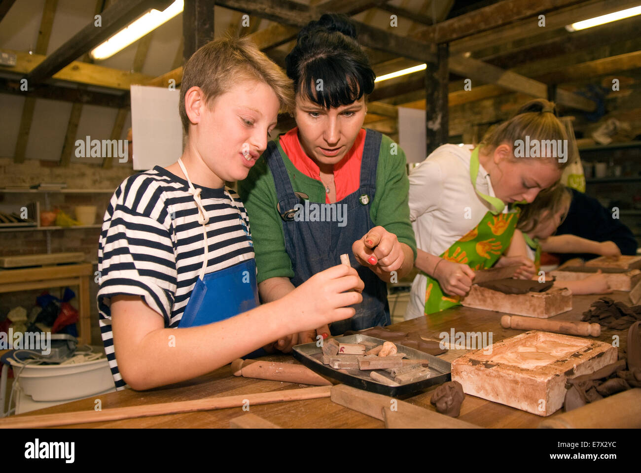 Kids receiving help from tutor (middle) whilst learning brick rolling at a heritage and demonstration day at local pottery... Stock Photo