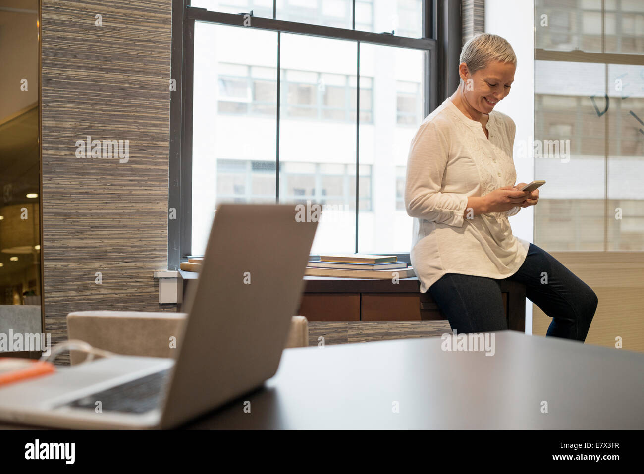 Office life.A woman seated on the edge of her desk using a digital tablet. Stock Photo