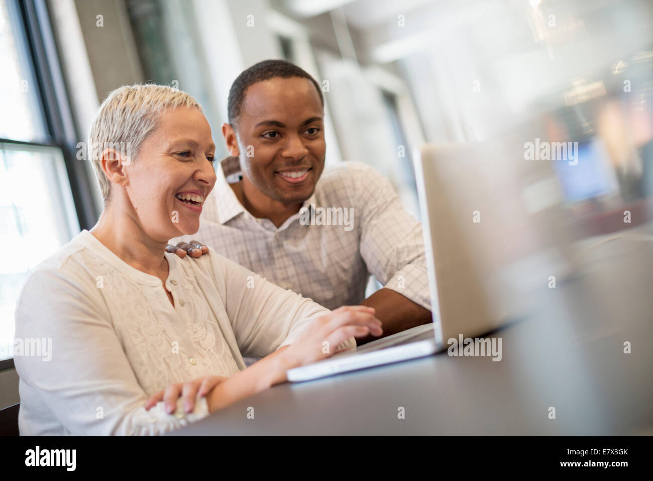 Office life. Two people, a man and woman looking at a laptop screen and laughing. Stock Photo