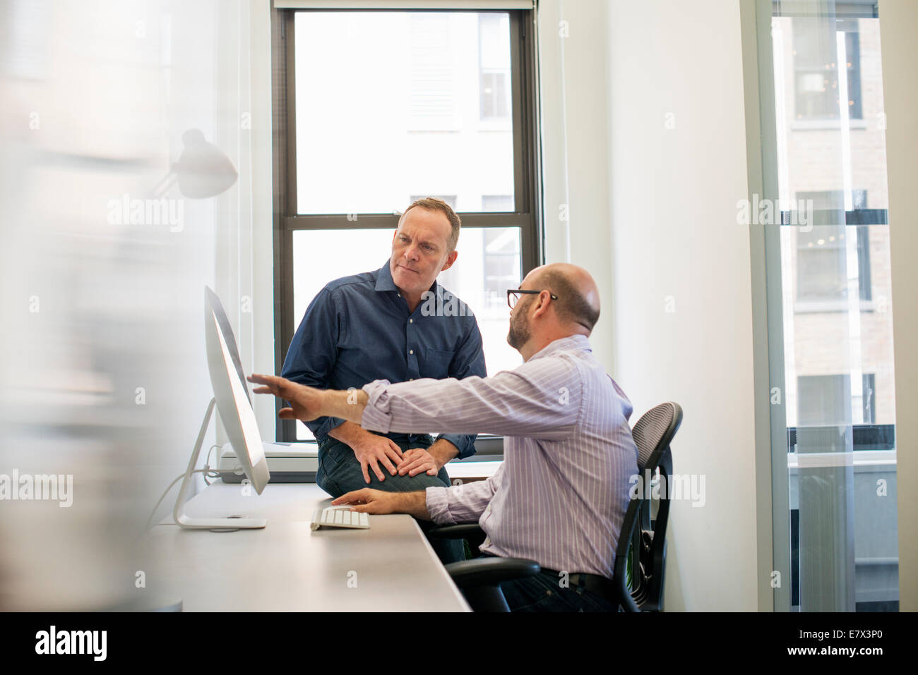 Two business colleagues in an office talking and referring to a computer screen. Stock Photo