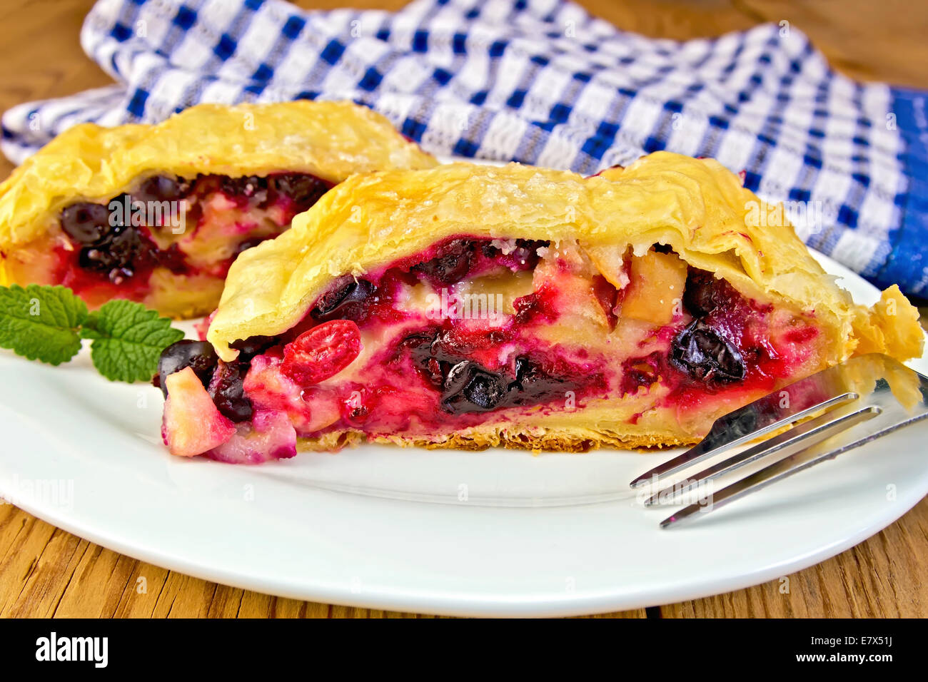 Strudel with black currant and cherry on a plate, napkin on the background of wooden boards Stock Photo