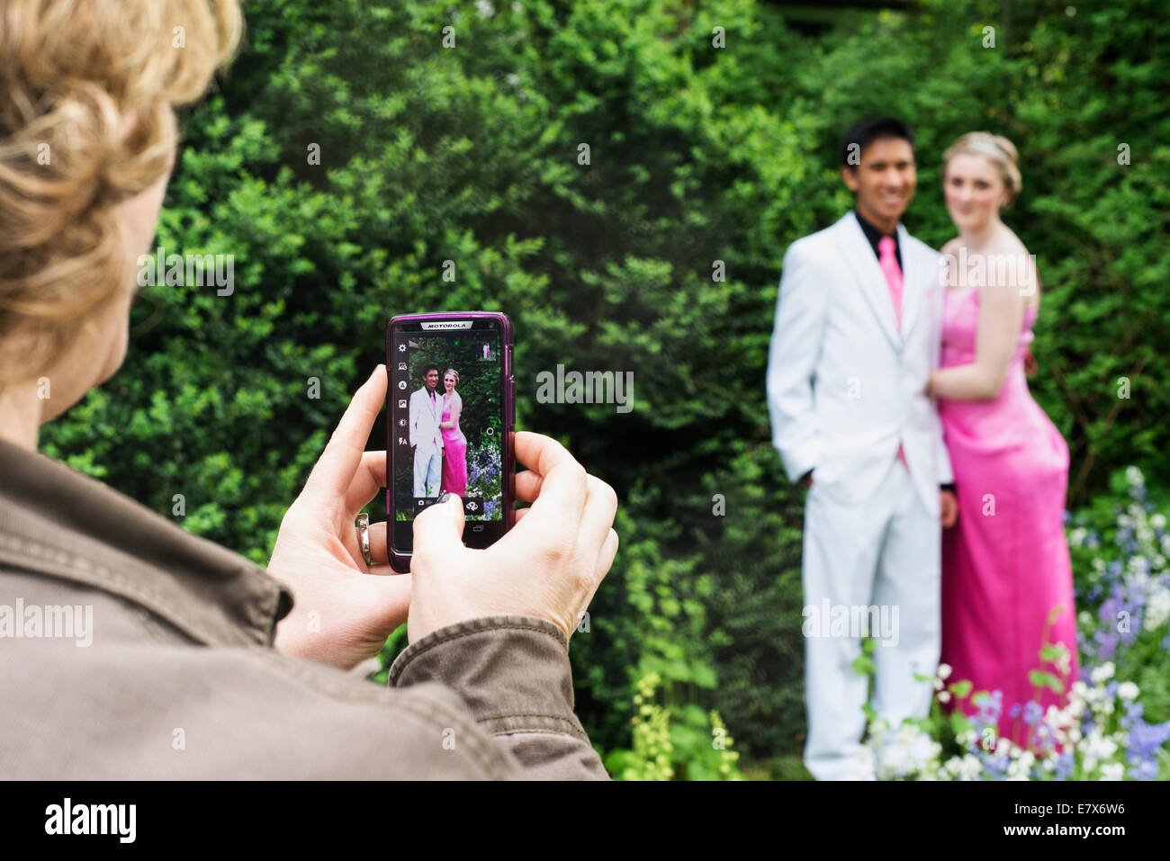 A mother taking a photograph of her daughter and prom date. Stock Photo