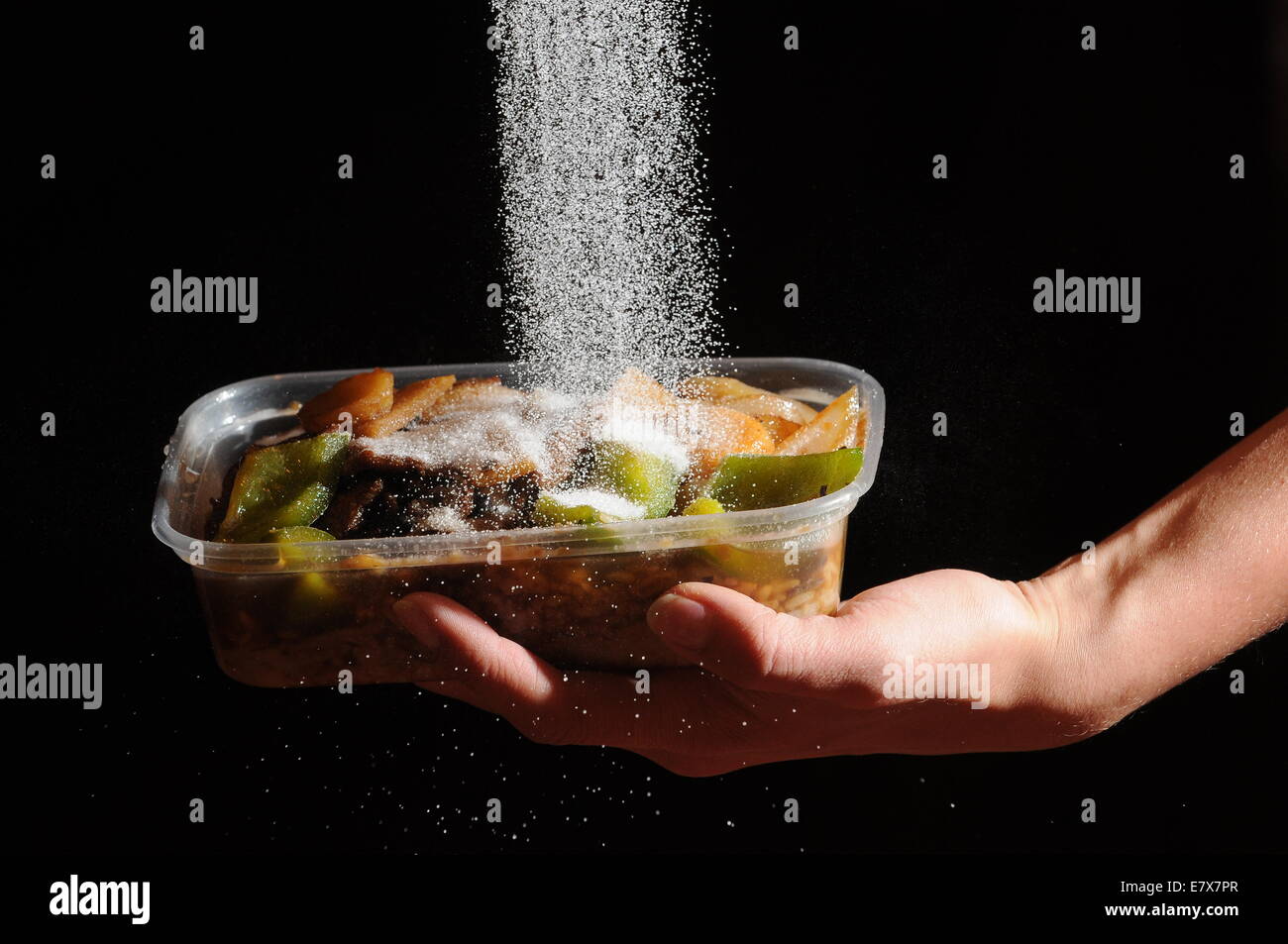 Takeaway food with salt being poured on from above. High levels of salt in junk food cause high blood pressure and heart disease Stock Photo