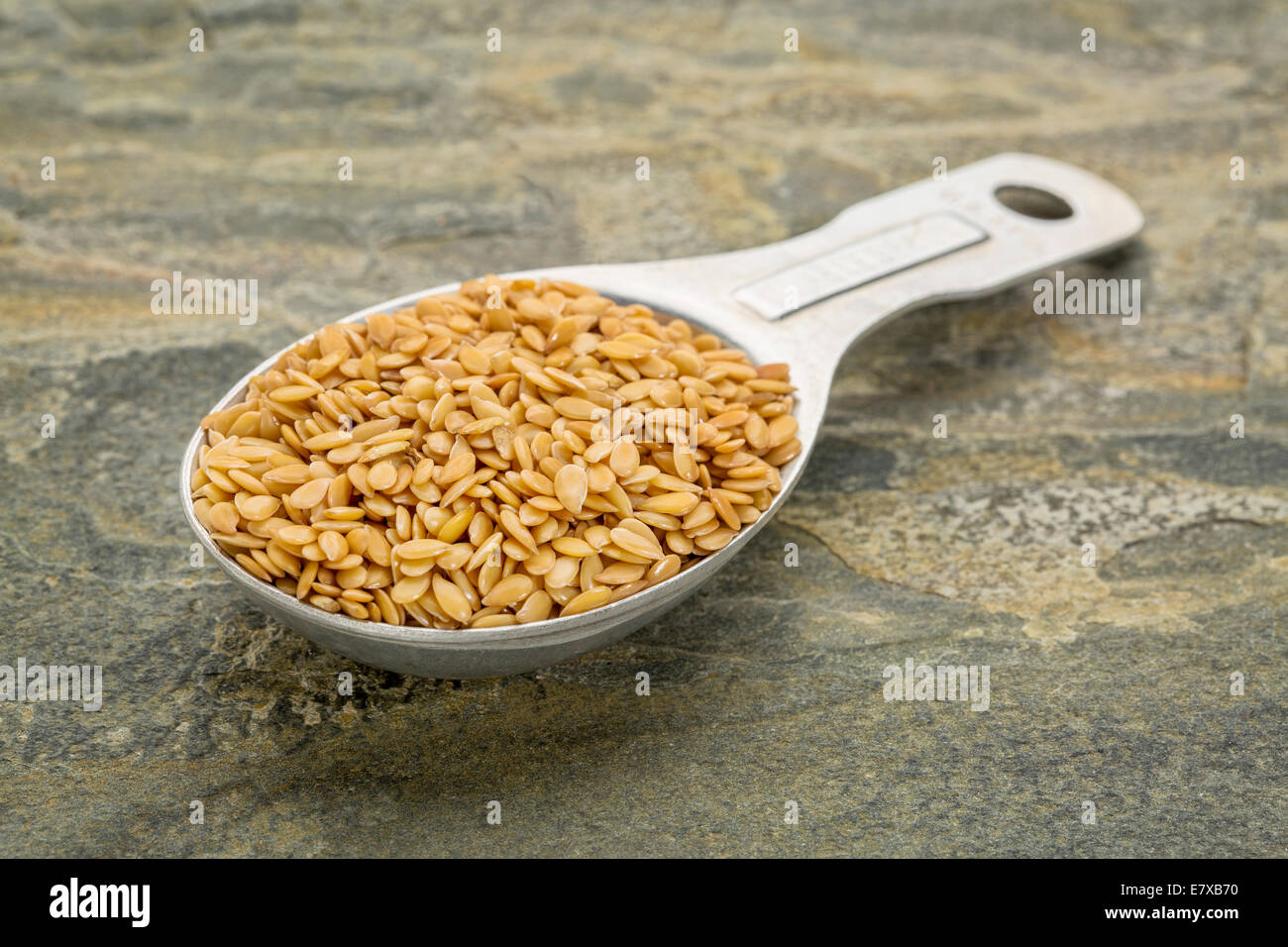 gold flax seeds in a measuring tablespoon against slate rock background