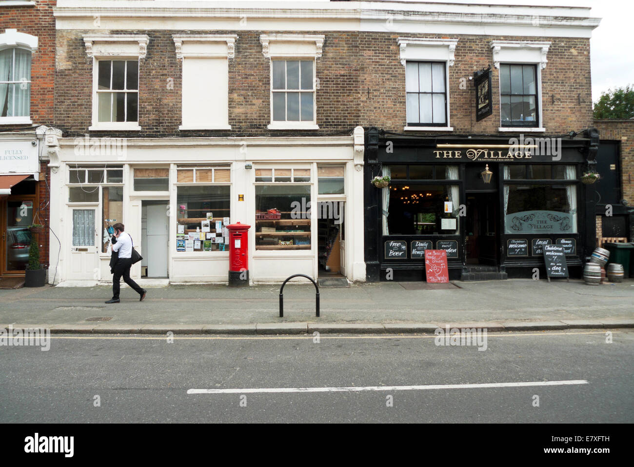 Boy walking past The Village pub and shops in Orford Road, Walthamstow
