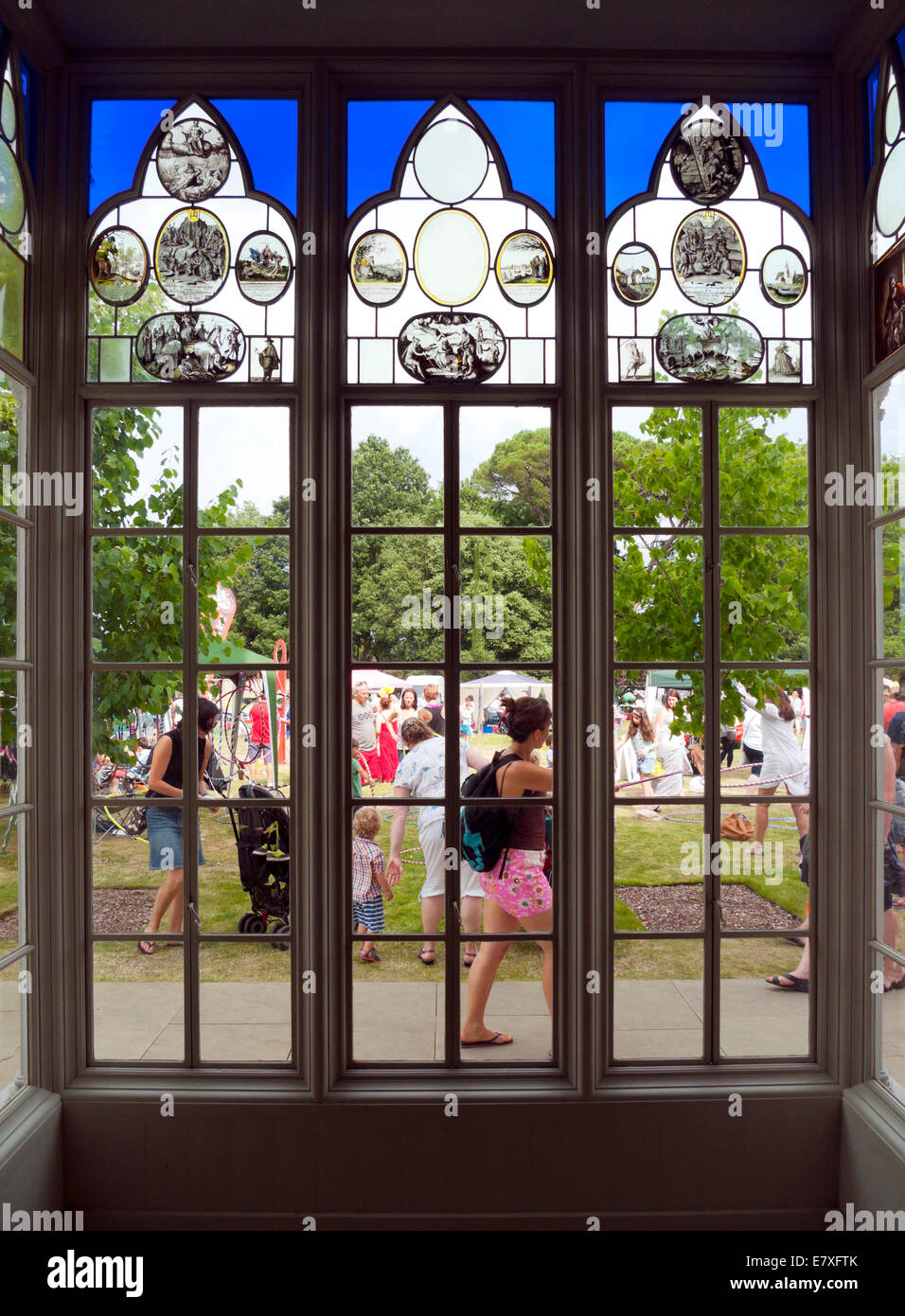 Garden Party Festival at Strawberry Hill House looking out of a stained glass window onto garden & people outside Twickenham in London UK KATHY DEWITT Stock Photo