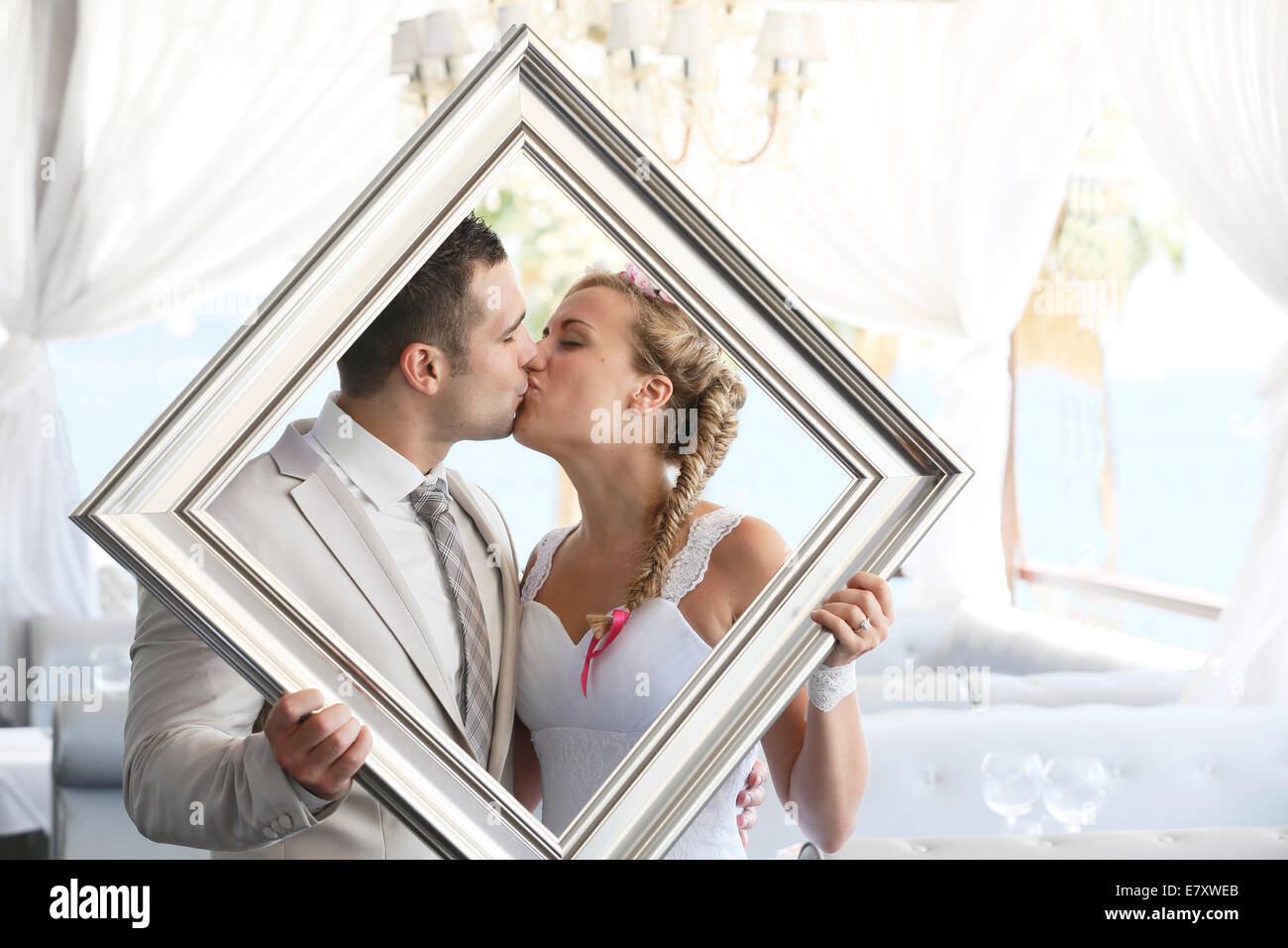 Bride and groom holding a picture frame in front of them, kissing, photo shoot Stock Photo